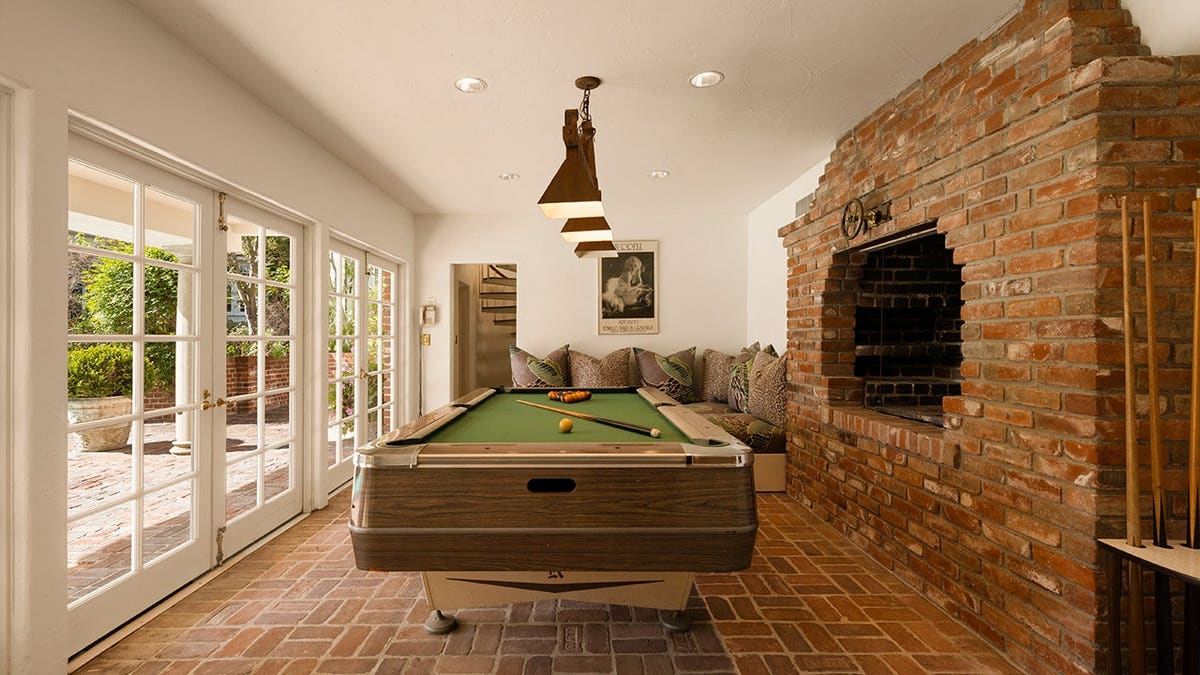 A room with brick floors and wall with a pool table and a fireplace.