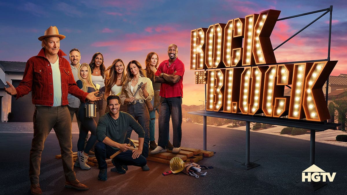 A group of home renovation hosts stand together on a suburban street at sunset beside a large illuminated 