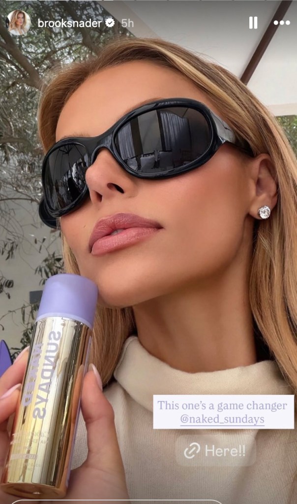 A woman wearing black sunglasses holding a Naked Sundays sunscreen product.