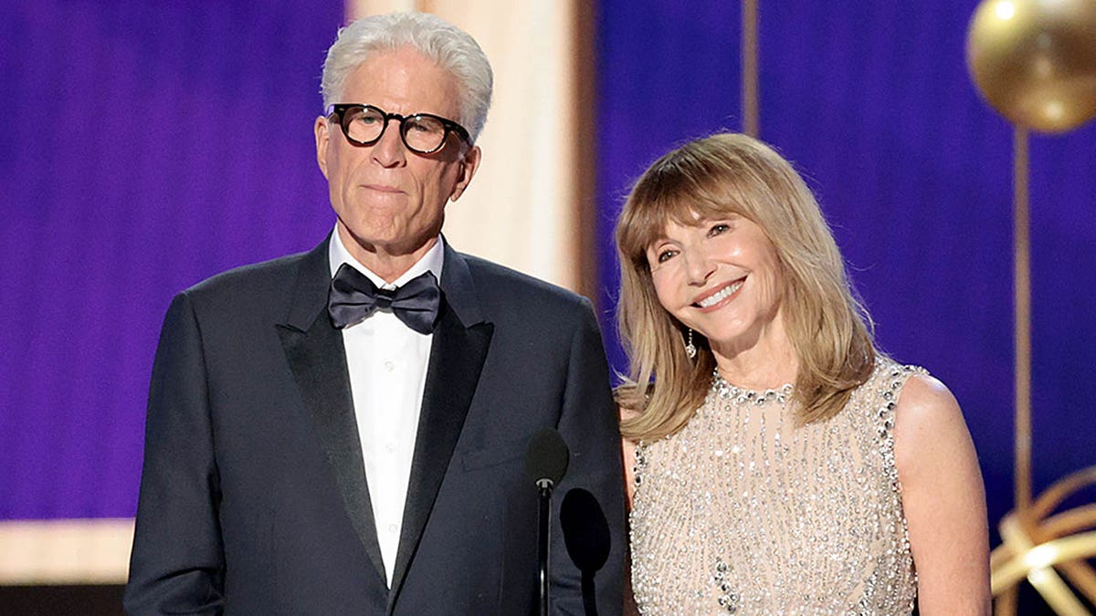 Ted Danson and Mary Steenburgen stand onstage at the Emmy Awards, with Mary smiling and Ted looking more serious