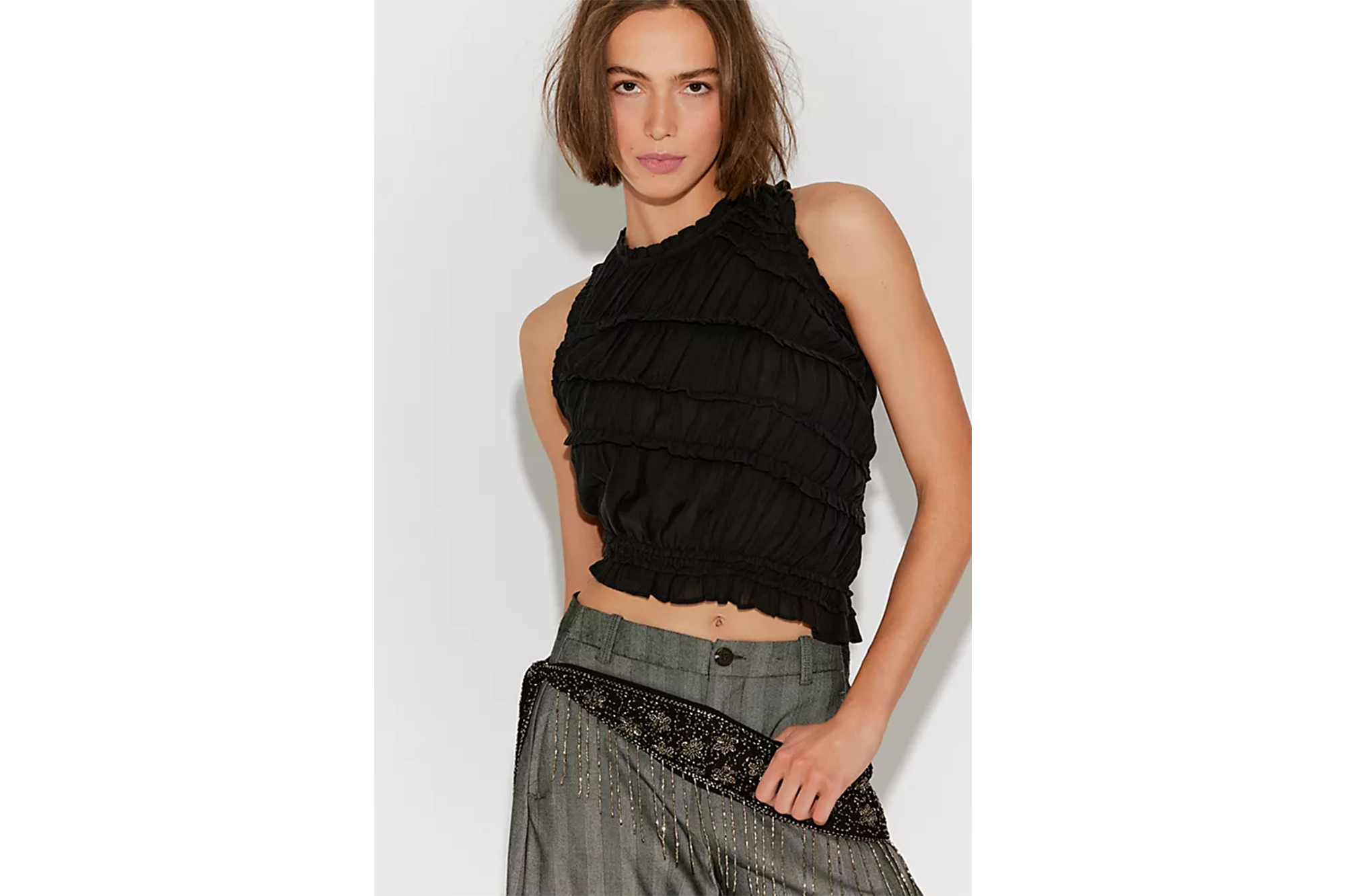 A woman in a black tiered halter top and grey pants with a decorative beaded belt.
