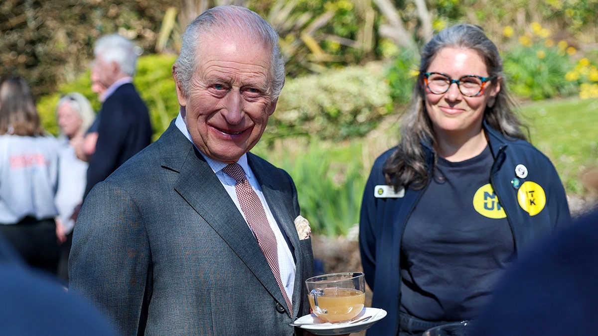 King Charles III smiling and holding tea at Seven Sisters National Nature Reserve reception