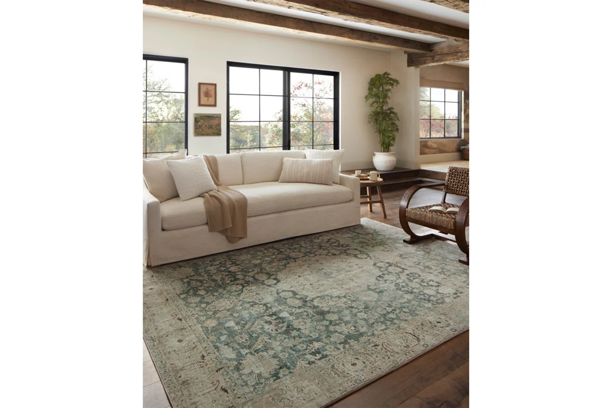 A living room with a cream sofa, a wooden rocking chair, and a patterned teal and beige rug.