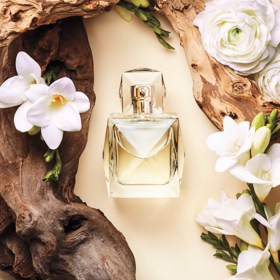 A bottle of XO Khloe fragrance surrounded by white flowers and driftwood.