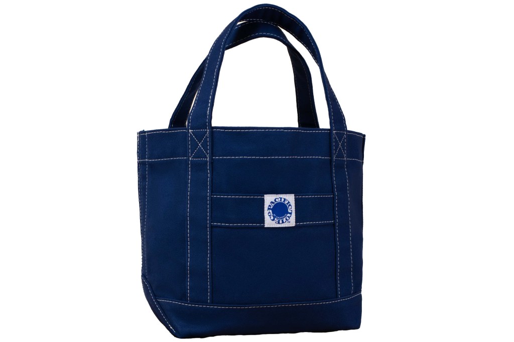 A blue canvas tote bag with white stitching and a small circular "Pacific Tote Co." label.