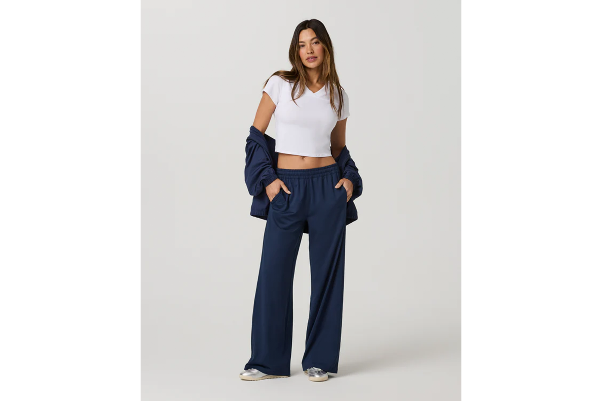 A woman wearing a white cropped V-neck t-shirt, navy wide-leg pants, and a matching navy jacket draped over her shoulders.