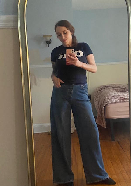 A woman taking a mirror selfie, wearing a black t-shirt and wide-leg jeans.