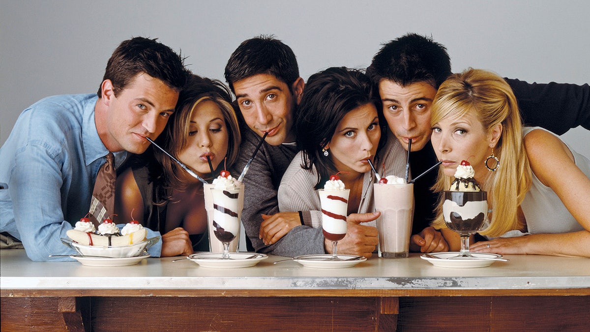The cast of Friends sitting behind a bar sipping milkshakes in a promo shot
