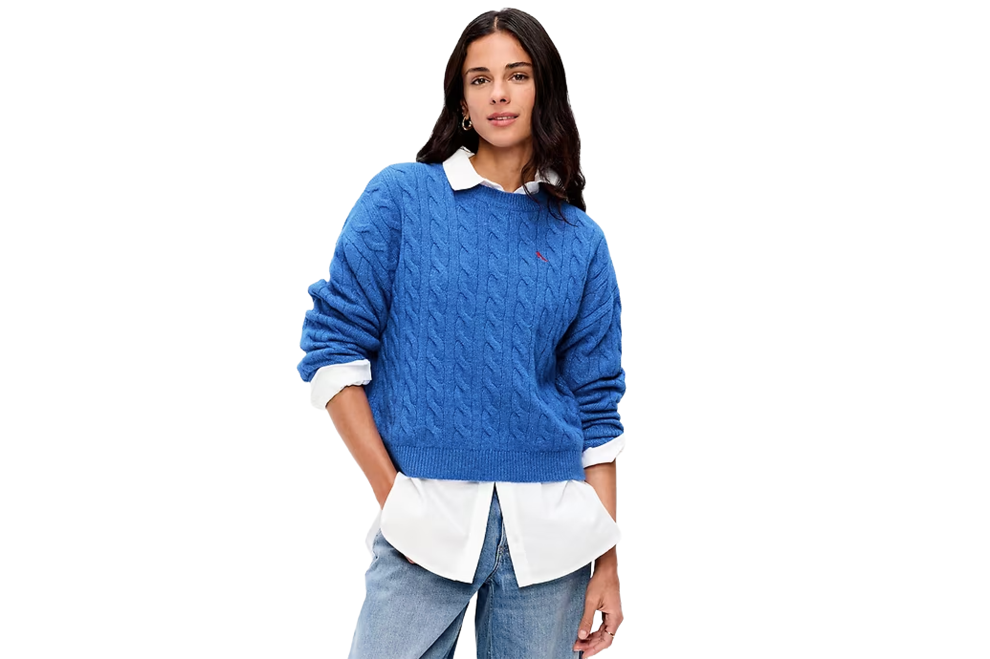 A woman wearing a blue cable-knit sweater over a white collared shirt and light-wash jeans.