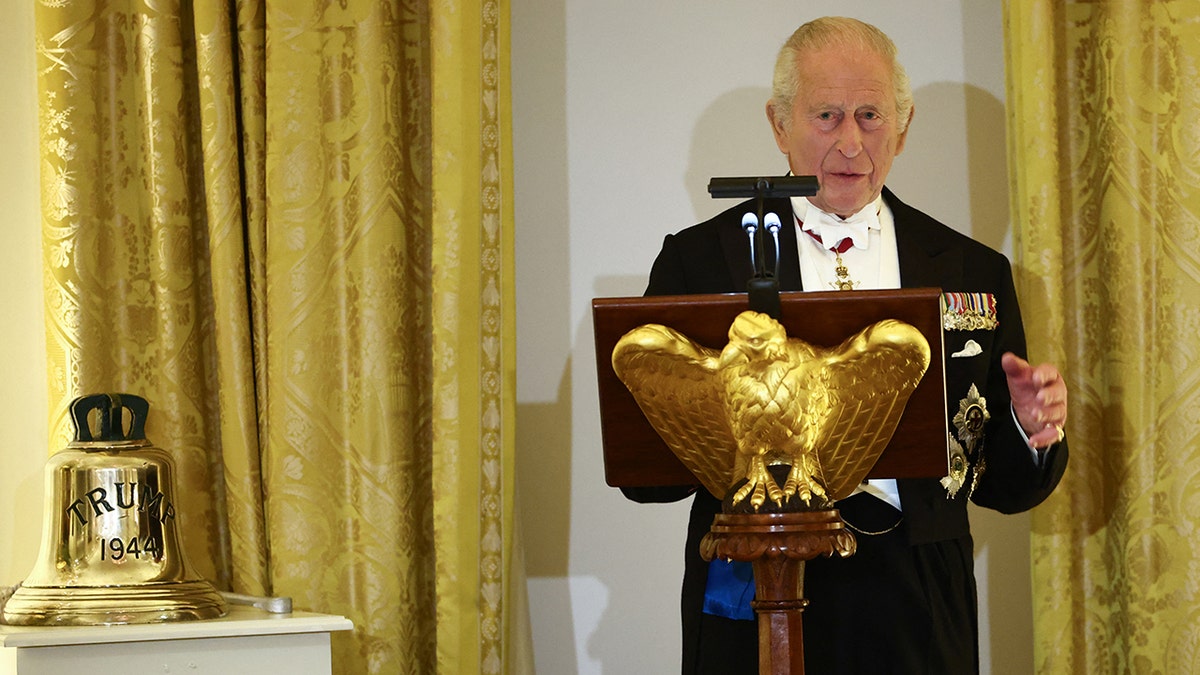 King Charles giving a speech next to a bell.