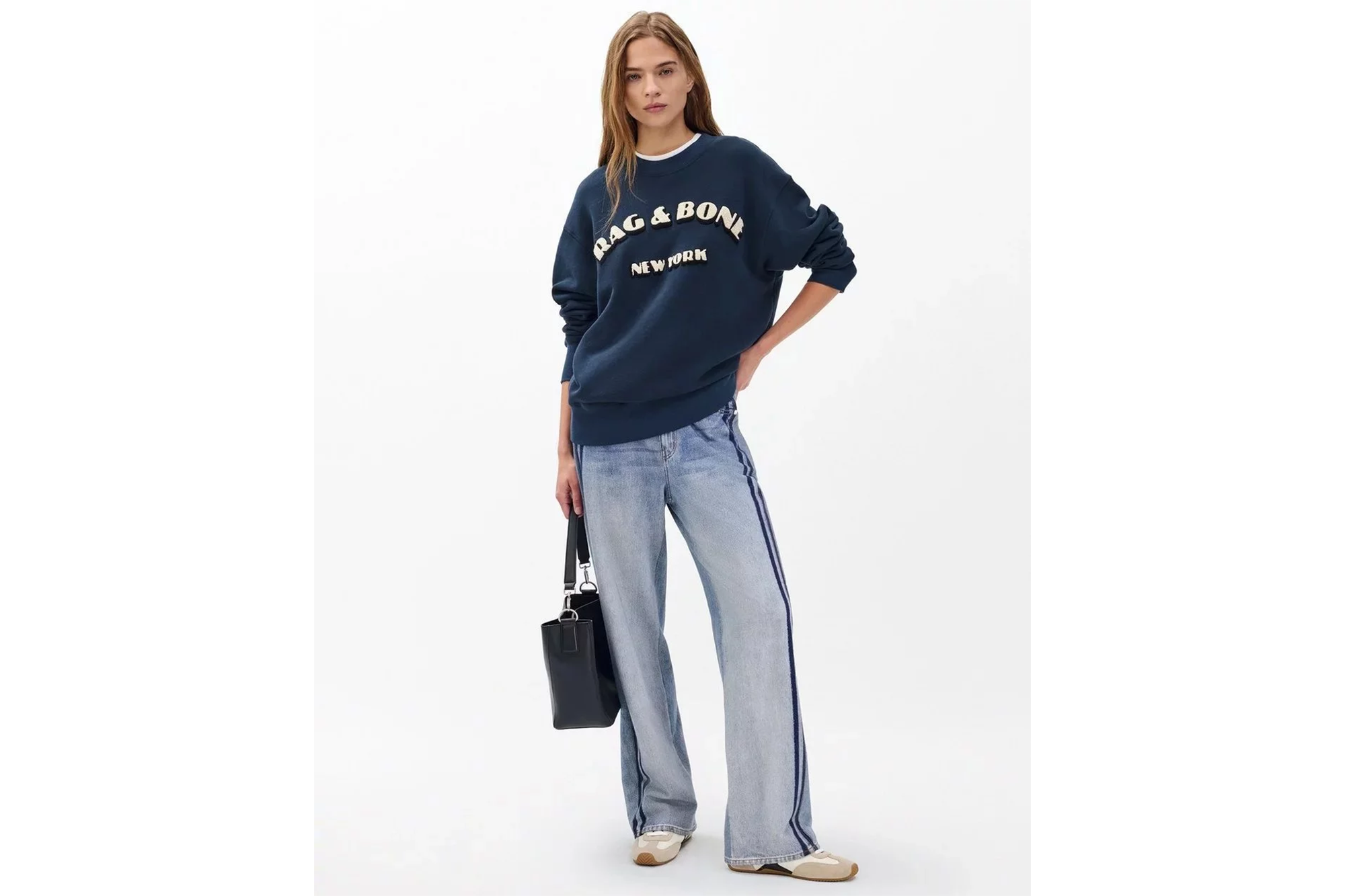 Woman wearing a navy blue Rag & Bone New York sweatshirt, light wash jeans with dark side stripes, and carrying a black handbag.