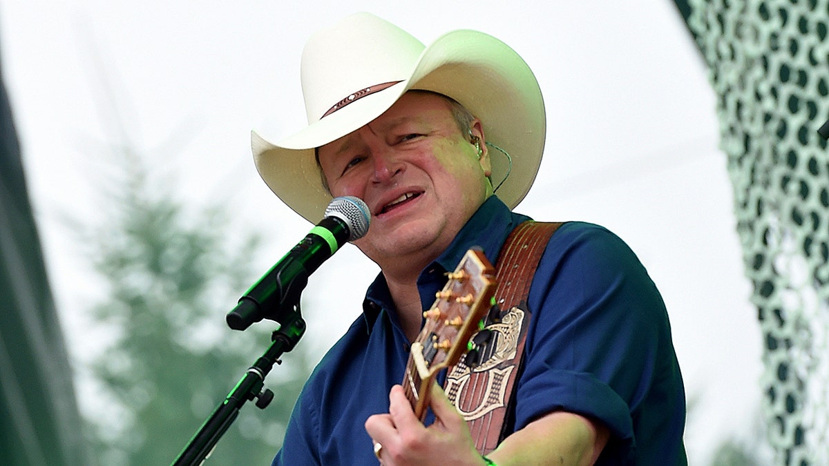 Mark Chesnutt wearing a cowboy hat and playing guitar while singing into microphone