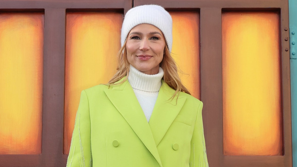 Jewel wearing a green coat and white beanie at the Macy's Thanksgiving Day Parade in New York City