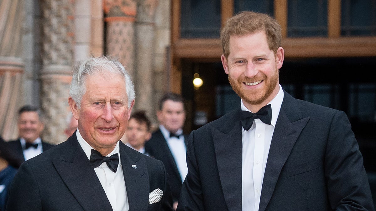 Prince Charles and Prince Harry standing together smiling in tuxedos at a red carpet event