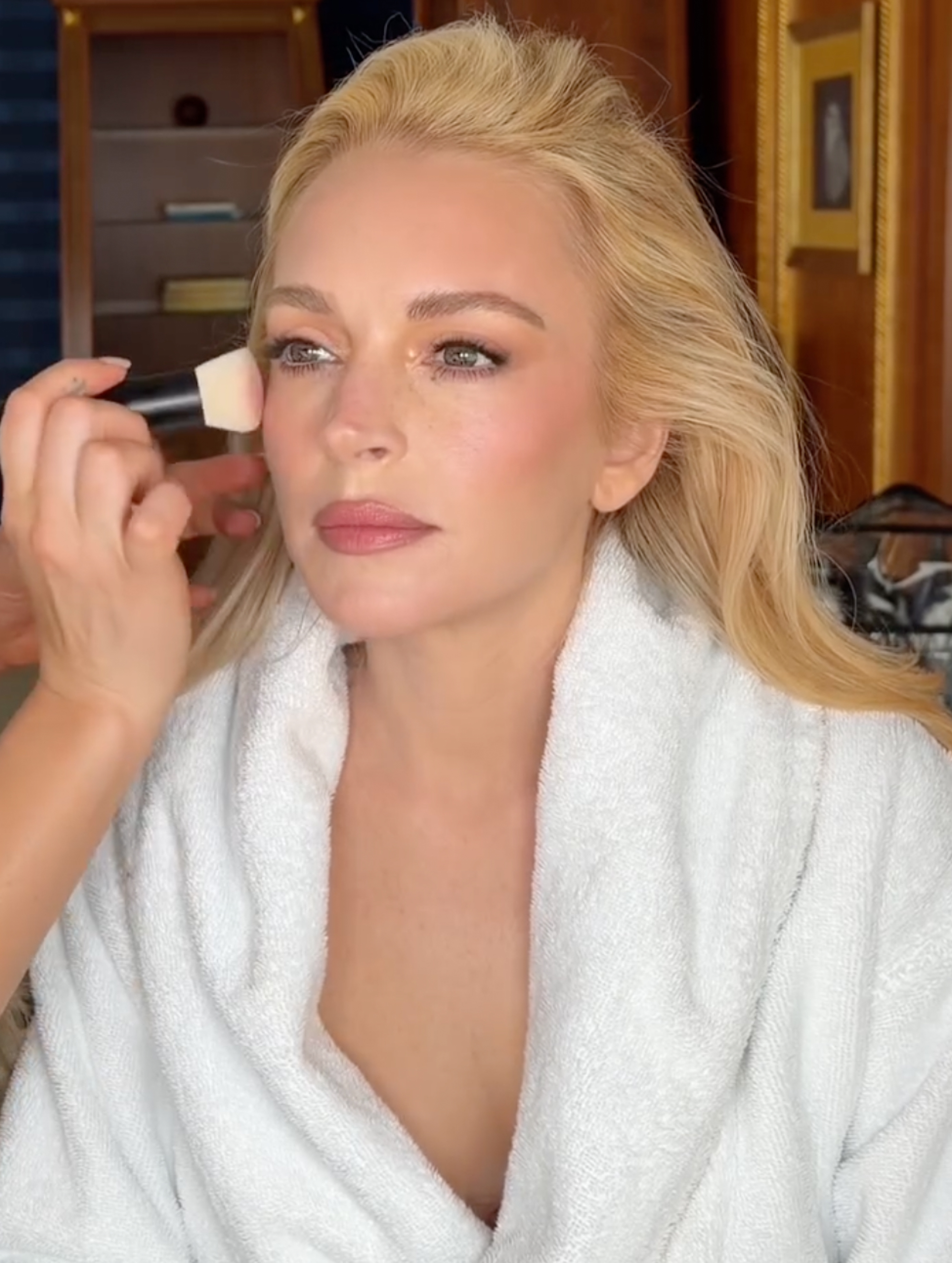 Lindsay Lohan getting makeup applied to her cheek.