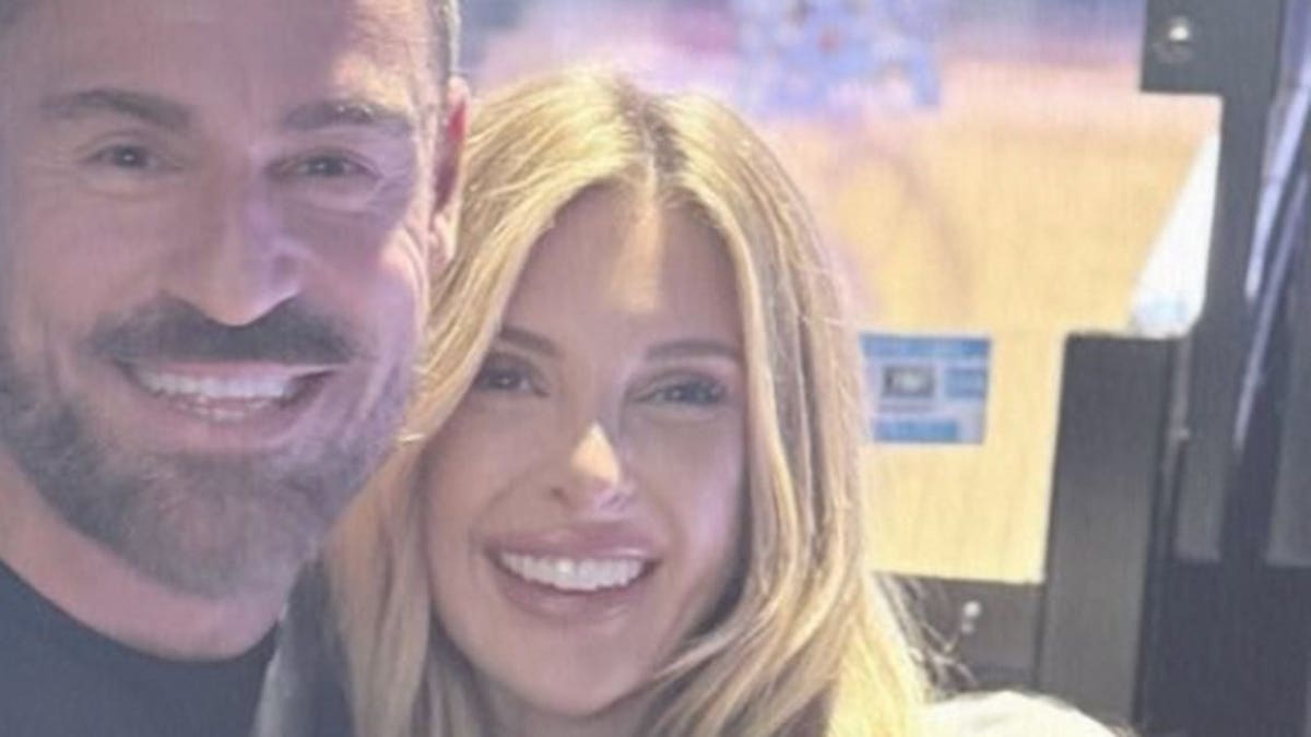 Close-up selfie of a smiling David Landsman and Lindsie Chrisley posing together indoors, with soft lighting and a blurred background.