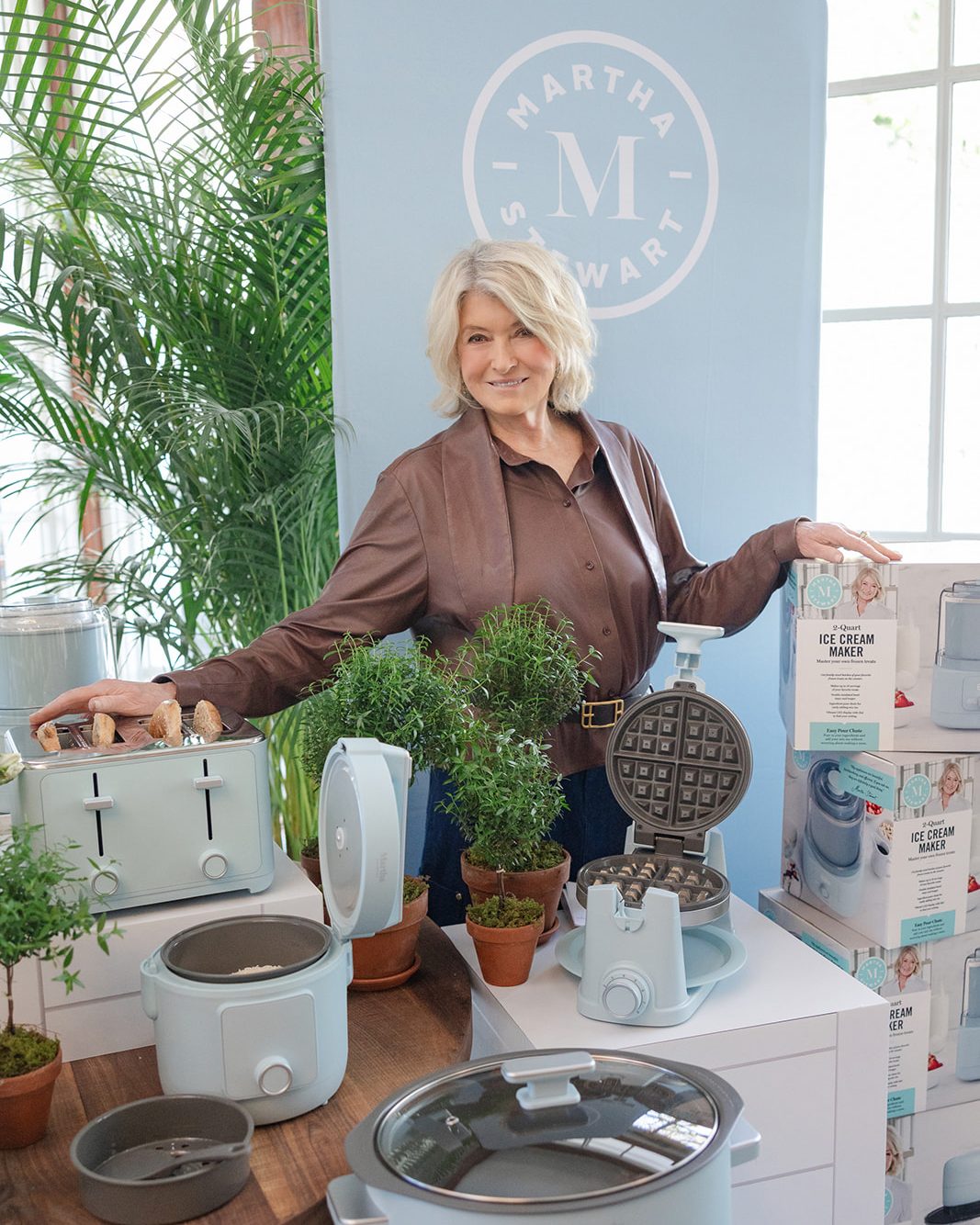 Martha Stewart poses with her new line of kitchen appliances in light blue, including a toaster, rice cooker, and waffle maker.