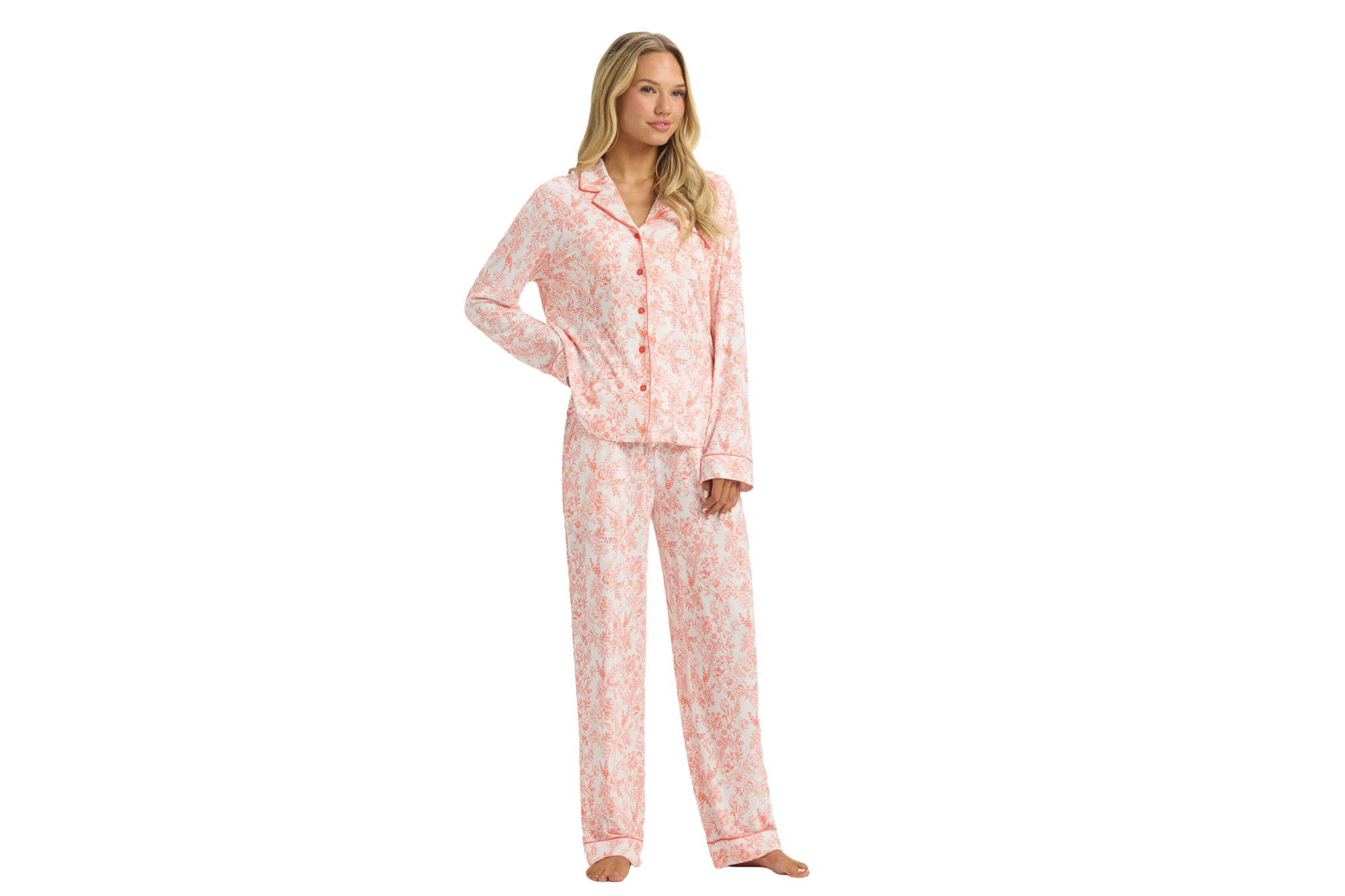 A woman poses wearing a two-piece peach-colored pajama set with a white floral pattern.