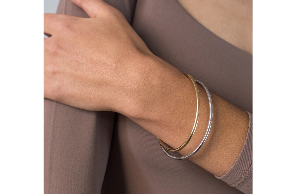 A person's arm wearing one gold and one silver bangle bracelet.