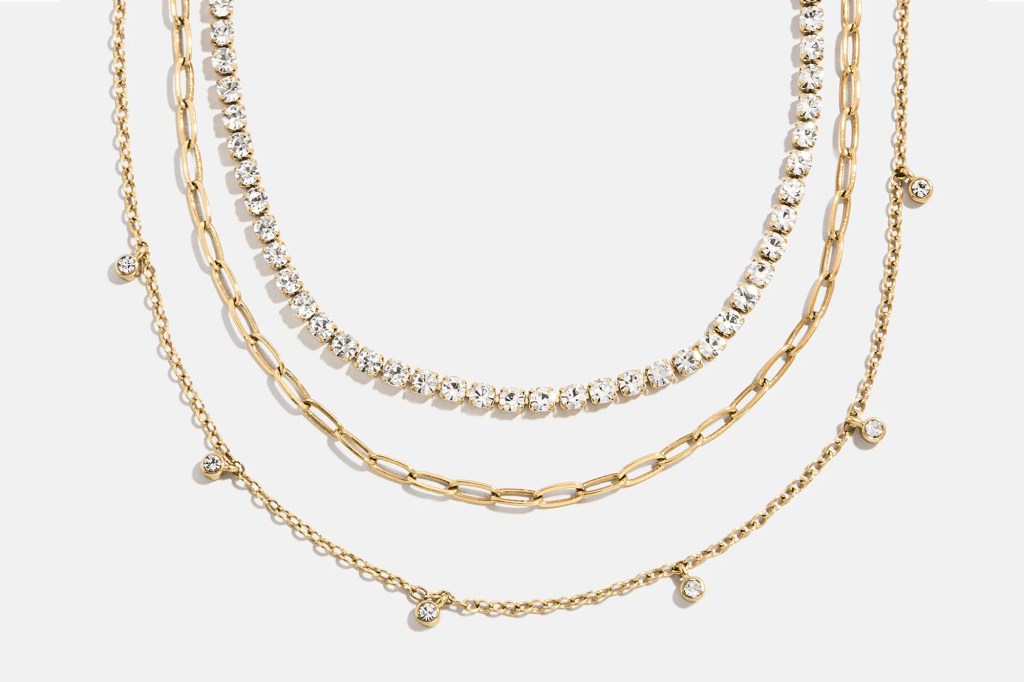 Three gold necklaces layered together, one with crystals, one a link chain, and one with small dangling crystals.