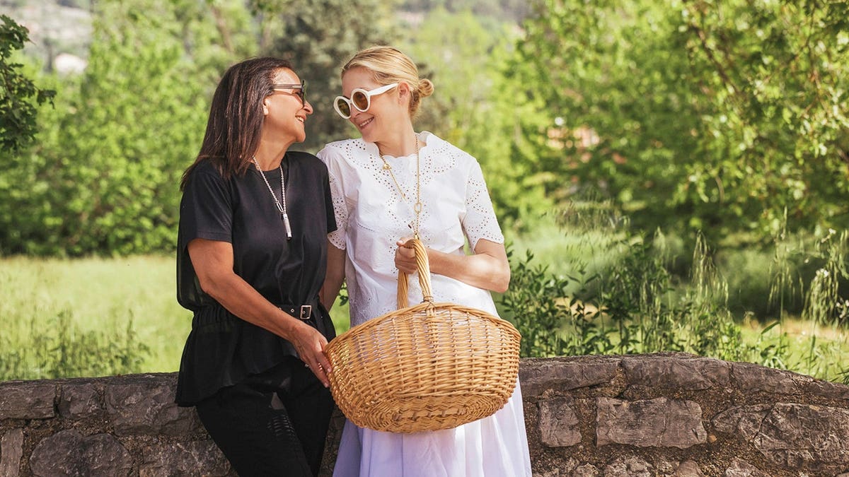 Kelly Rutherford in a white dress smiling in a floral field next to her friend Véronique Gabai.