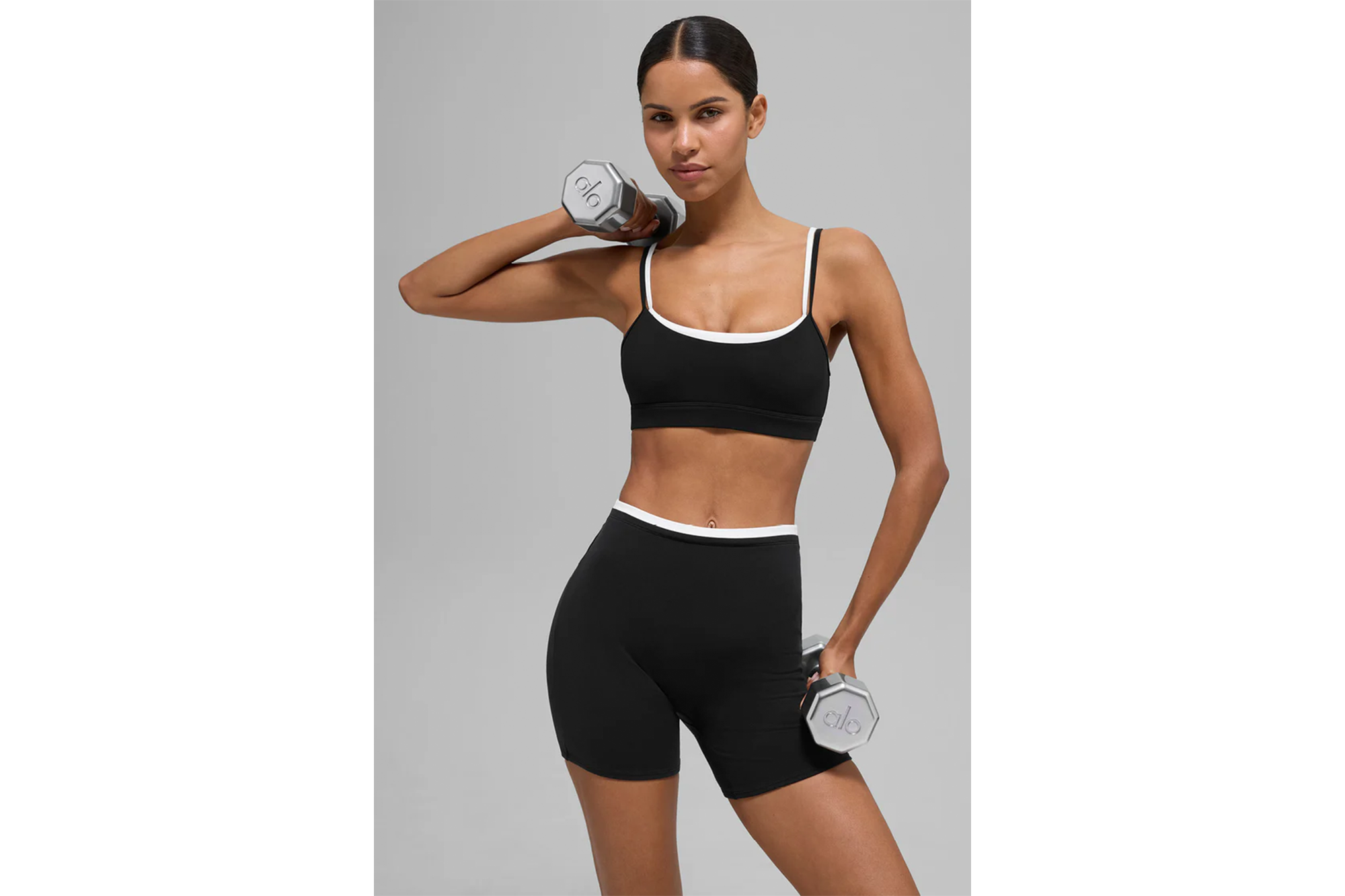 Woman in black sports bra and shorts holding dumbbells.