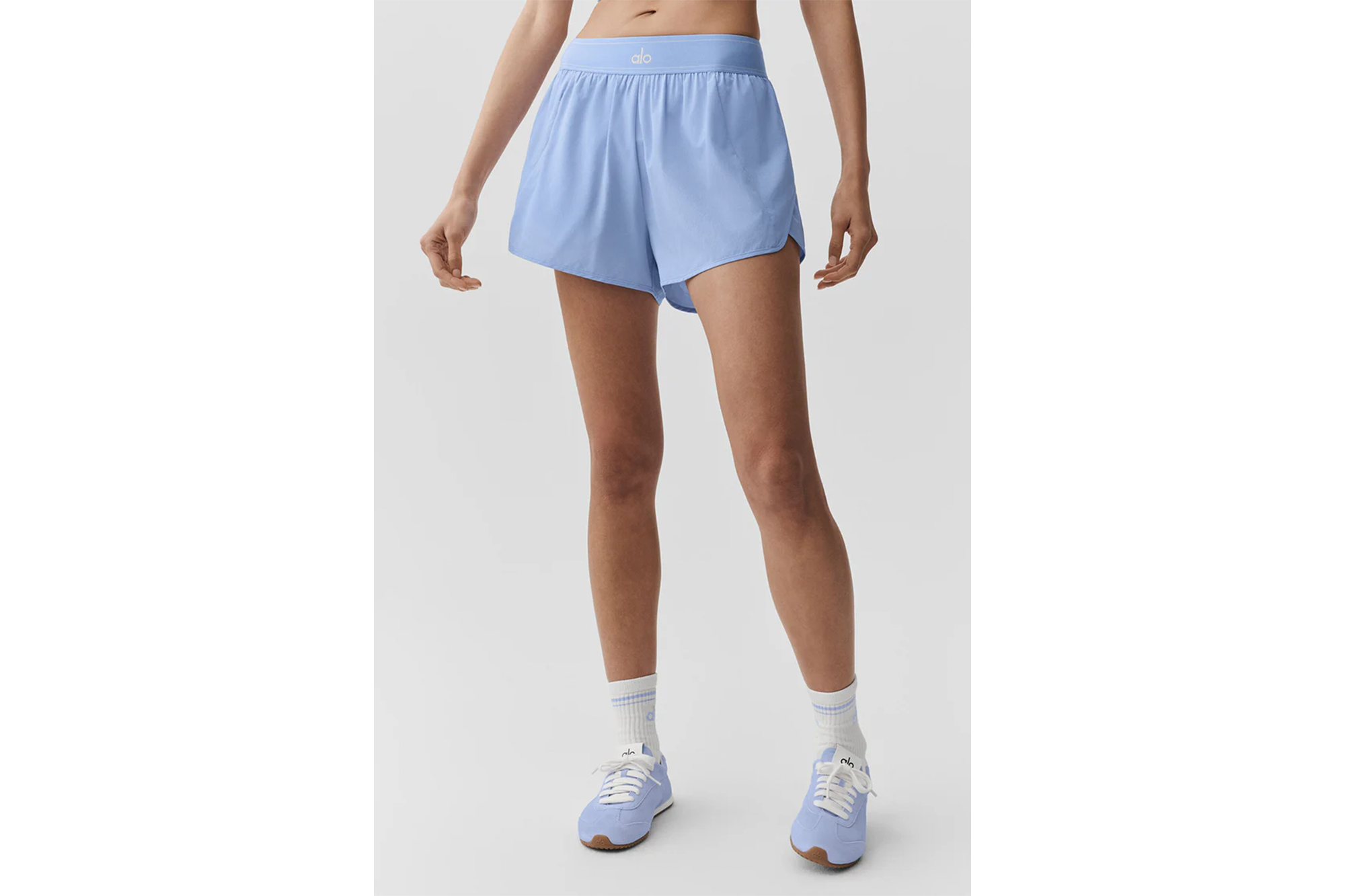 Woman wearing light blue shorts, white socks with blue stripes, and light blue sneakers.