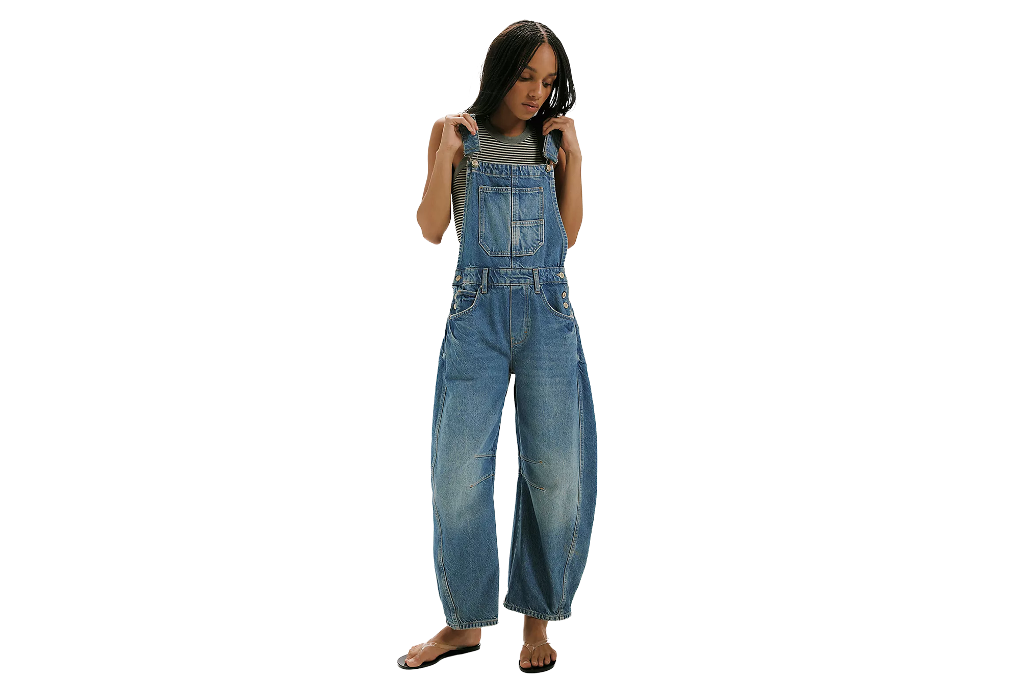 A woman wearing a striped top, denim overalls, and black flip-flops.