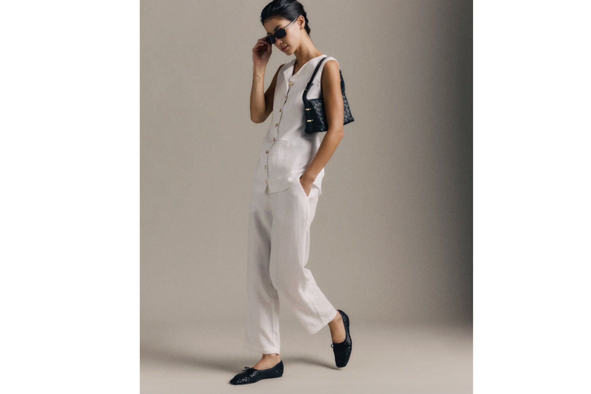 A woman modeling a white sleeveless top, matching pants, black woven flats, and a black woven shoulder bag.