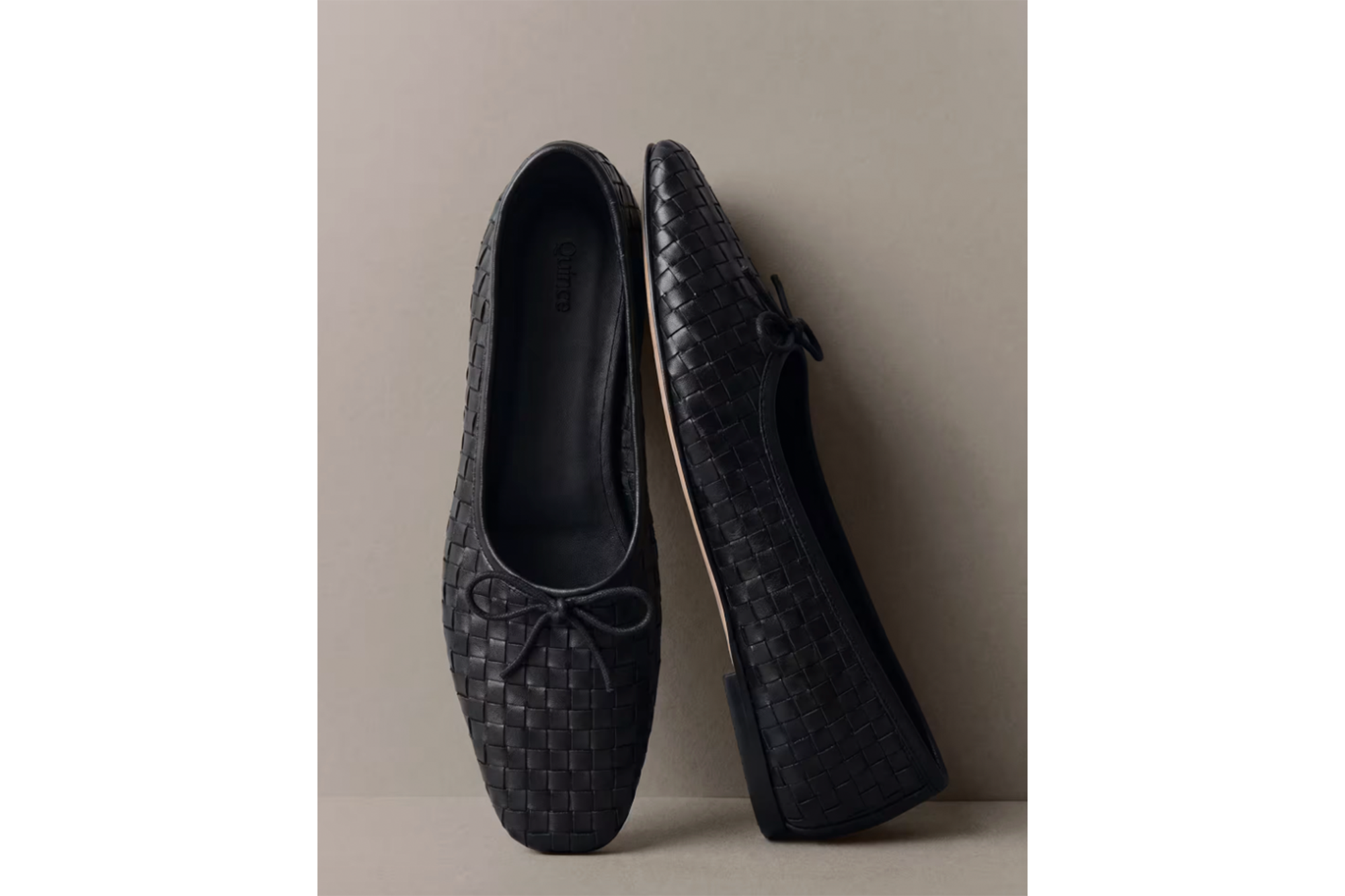 A pair of black woven leather ballet flats with small bows.