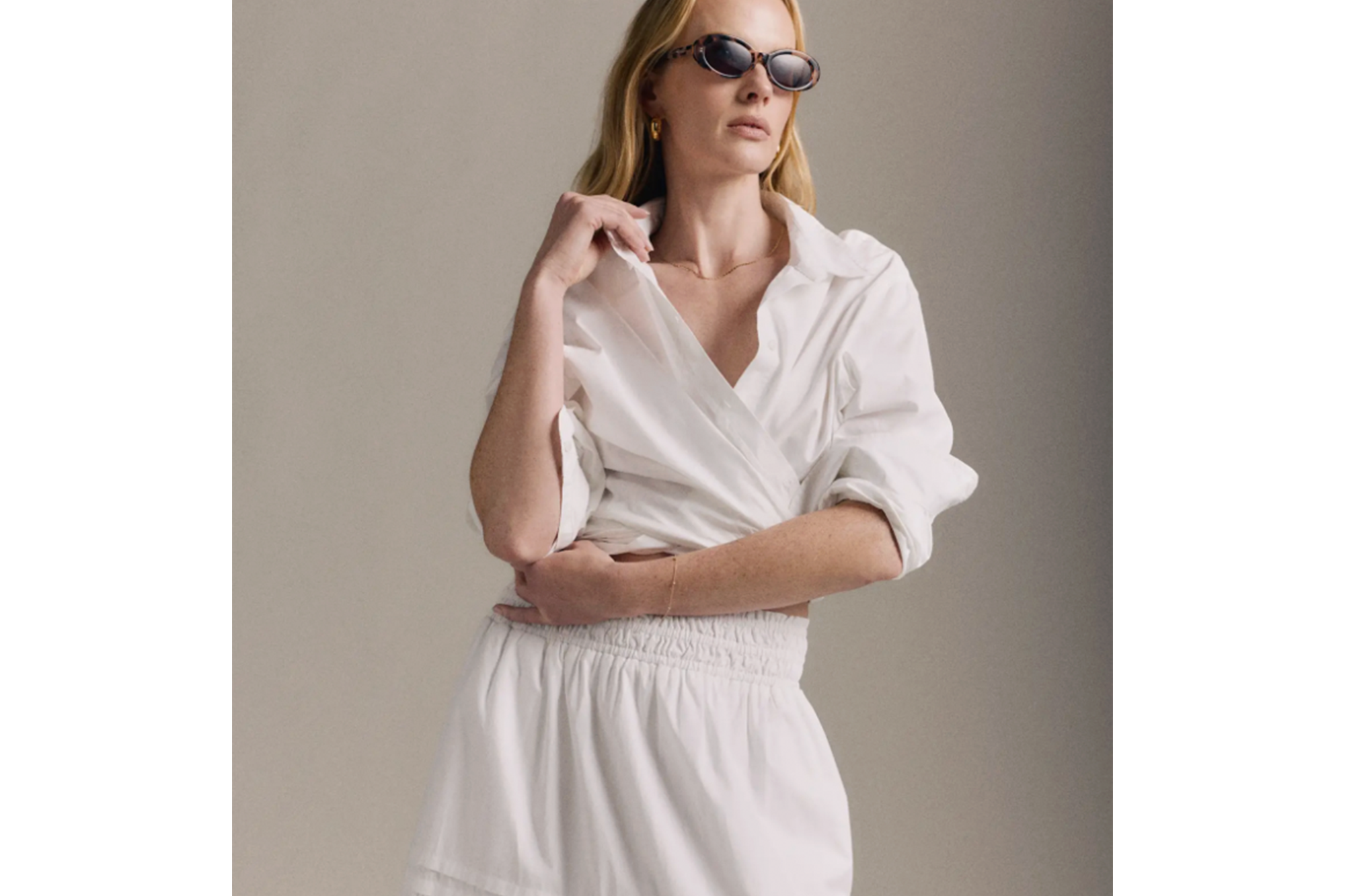 A blonde woman in a white wrap shirt, white shorts, and sunglasses.