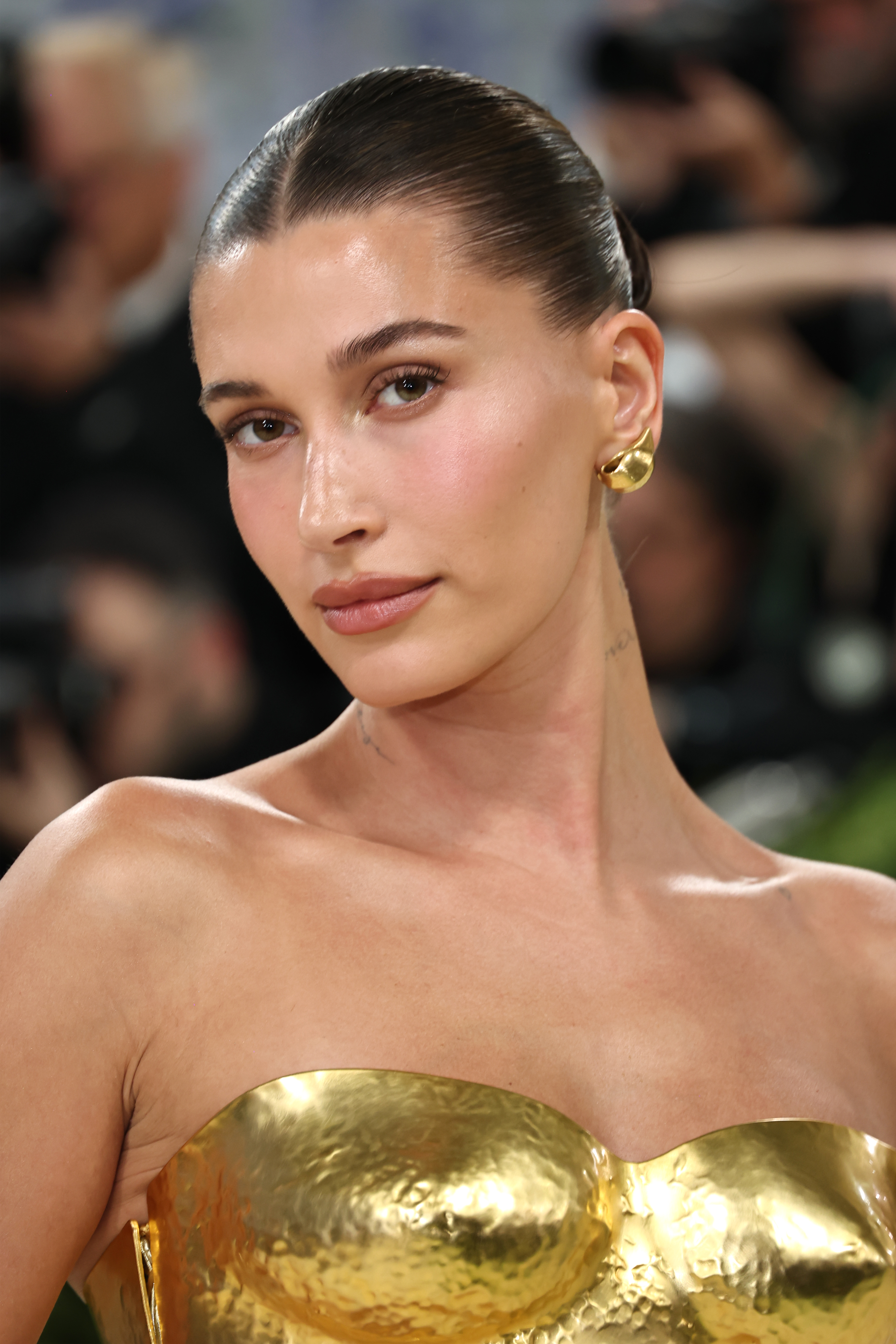 Hailey Bieber wearing a golden strapless gown and golden earrings at the 2026 Met Gala.