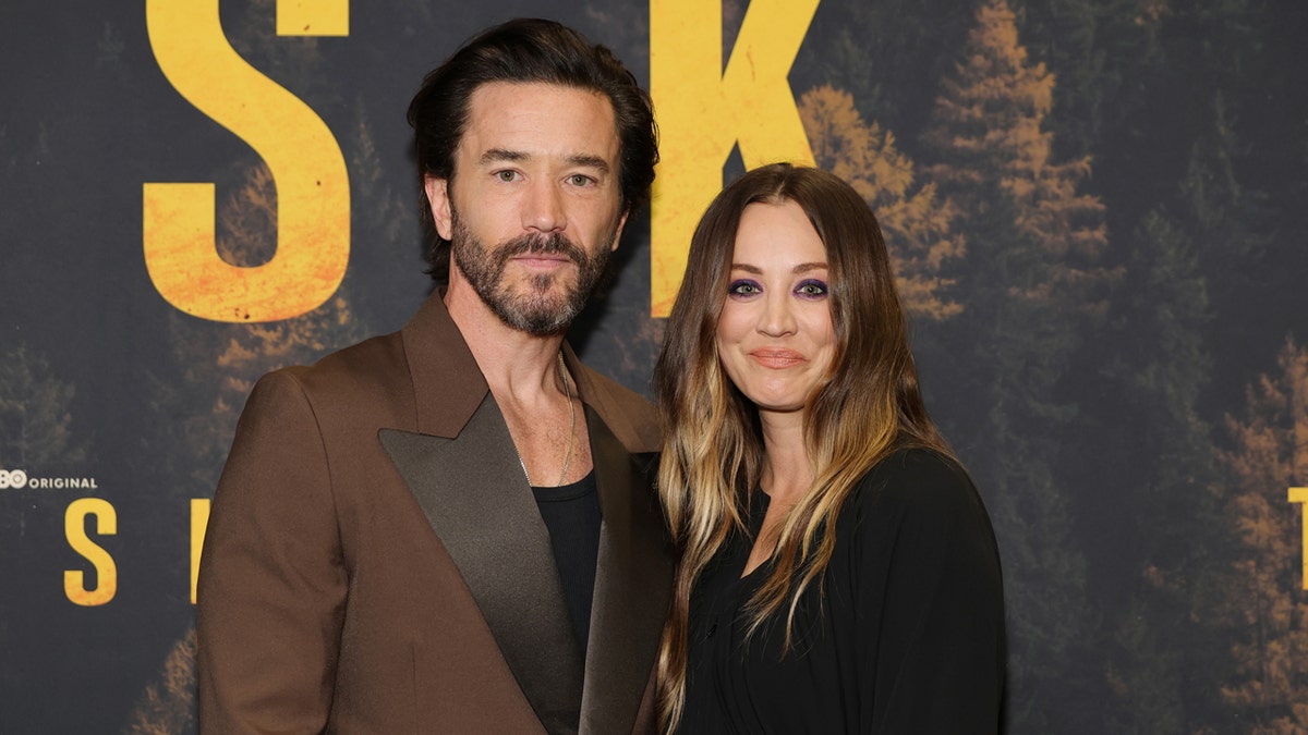 Tom Pelphrey and Kaley Cuoco posing together on a red carpet at the Perelman Performing Arts Center.
