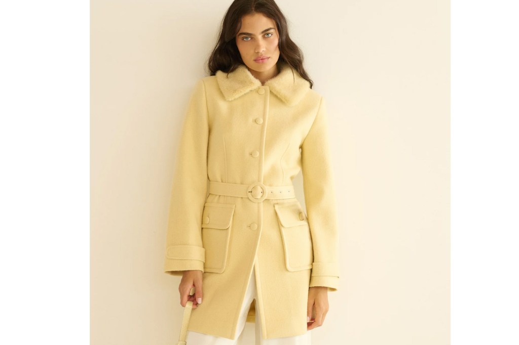 A woman wearing a yellow coat with a belt and fur collar.