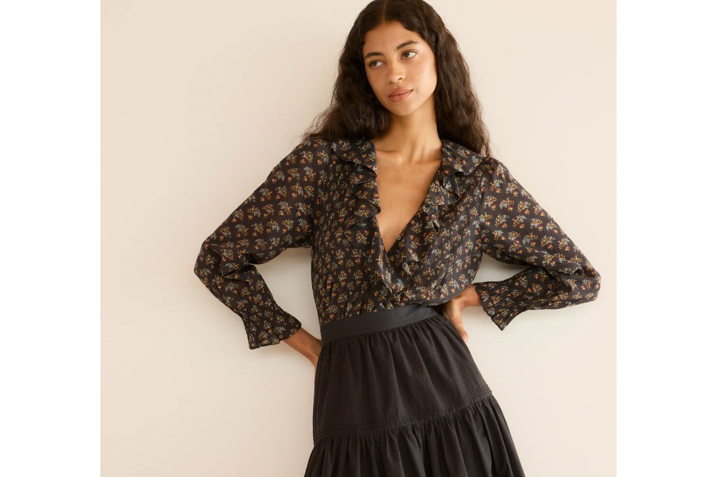 Woman wearing a dark floral blouse with ruffles and a black tiered skirt.