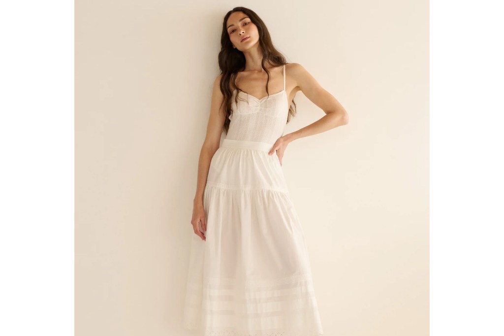 A model wearing a white camisole top and a tiered white maxi skirt with subtle striped and embroidered details.