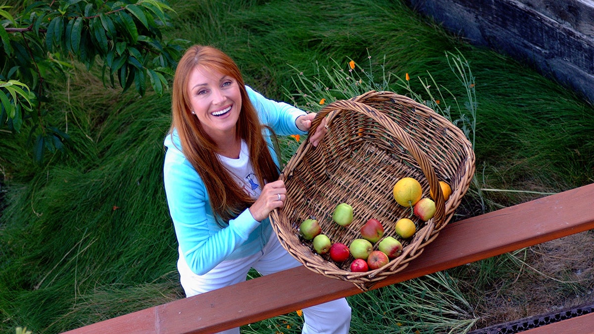 Actress Jane Seymour standing on deck of home holding wicker basket with apples