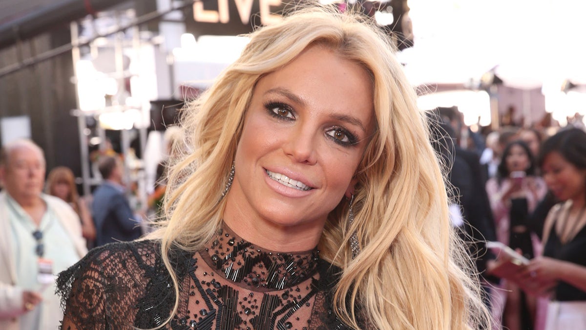 Britney Spears wearing a sheer black dress on a red carpet at an awards show