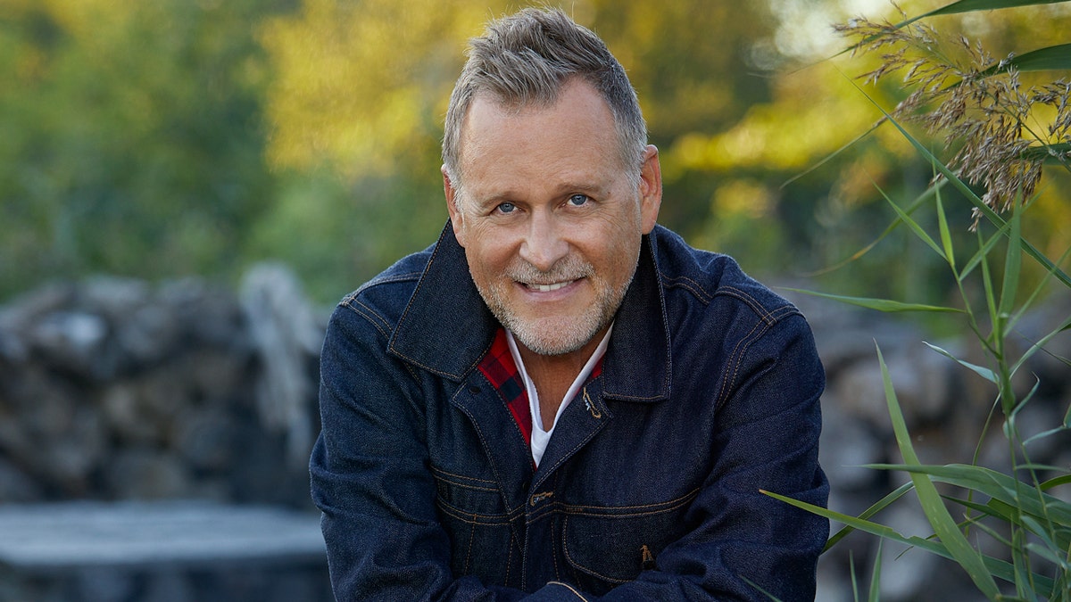 Dave Coulier sits by a fire outside