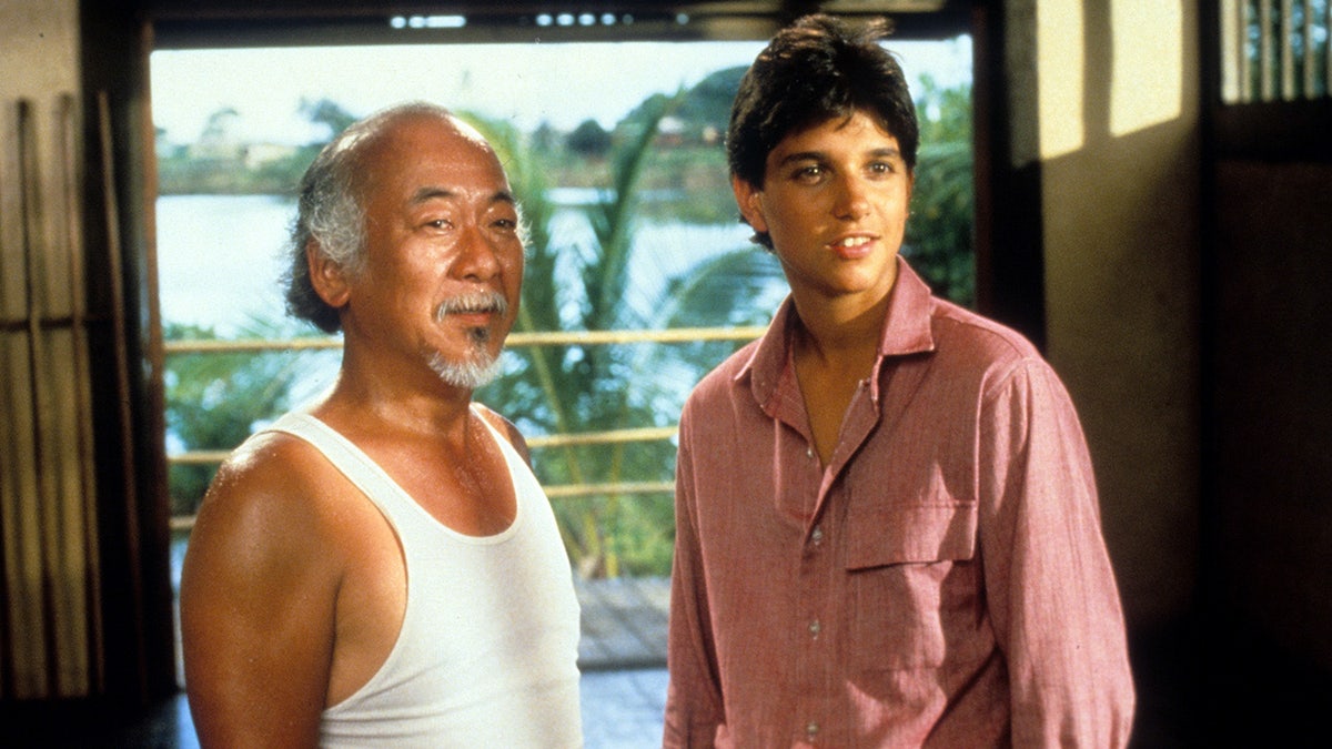 Pat Morita and Ralph Macchio sitting together in a scene from The Karate Kid film.